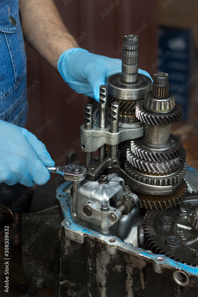 Naprawa mechanicznej skrzyni biegów samochodu przez mechanika. Rozkręcanie kluczem nasadowym uszkodzonej skrzyni biegów.