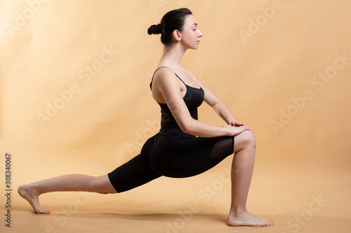 Side view portrait of beautiful young woman wearing white tank top working out against orange background, doing stretching.