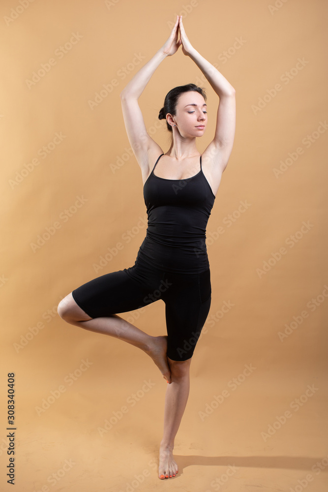 Side view portrait of beautiful young woman wearing white tank top working out against orange background, doing stretching.