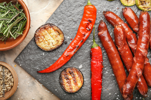 Tasty grilled sausages with vegetables on slate plate