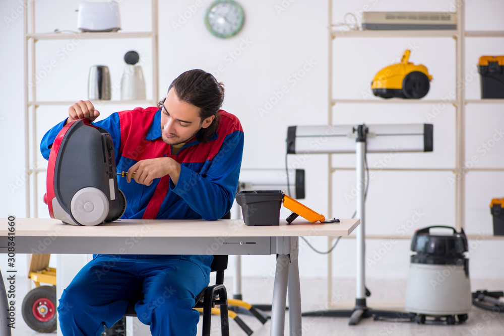 Young male contractor repairing vacuum cleaner at workshop Young male contractor repairing vacuum cleaner at workshop