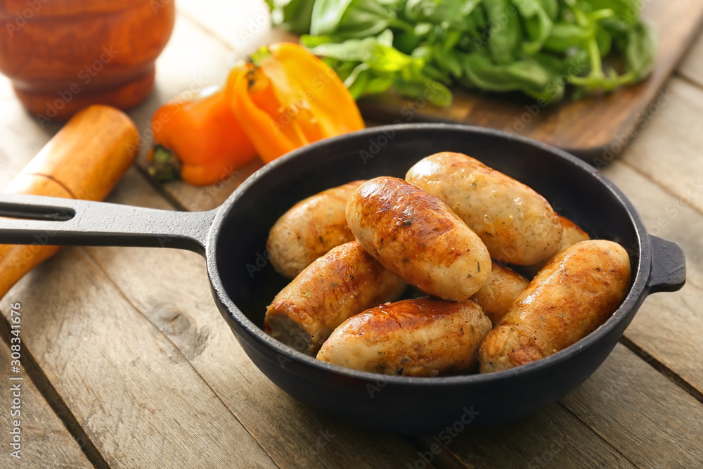 Frying pan with tasty grilled sausages on wooden table Frying pan with tasty grilled sausages on wooden table