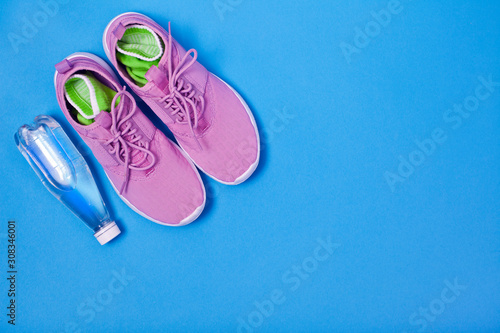 Pink sport shoes and bottle of water on a blue background. Concept healthy lifestyle, sport and diet. 