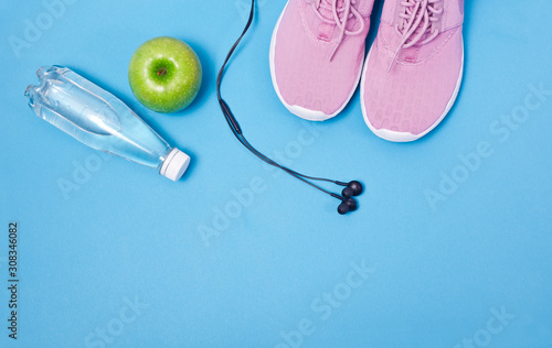 Pink sport shoes, earphones, green apple and bottle of water on a blue background. Concept healthy lifestyle, sport and diet. © Snowbelle