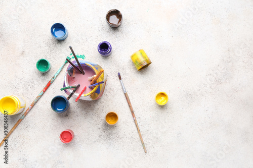 Jar with set of artist's brushes and paints on light background