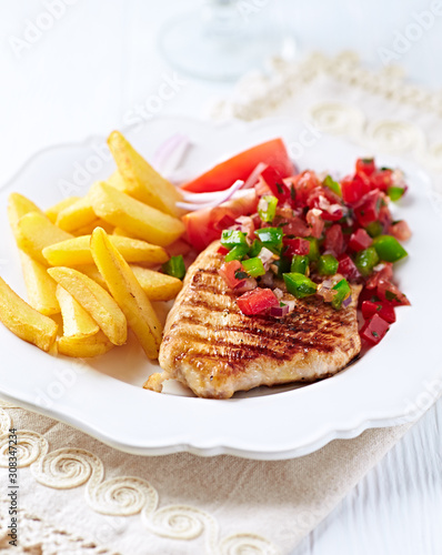 Grilled Turkey Breast with french fries and tomatoes. White wooden background. 