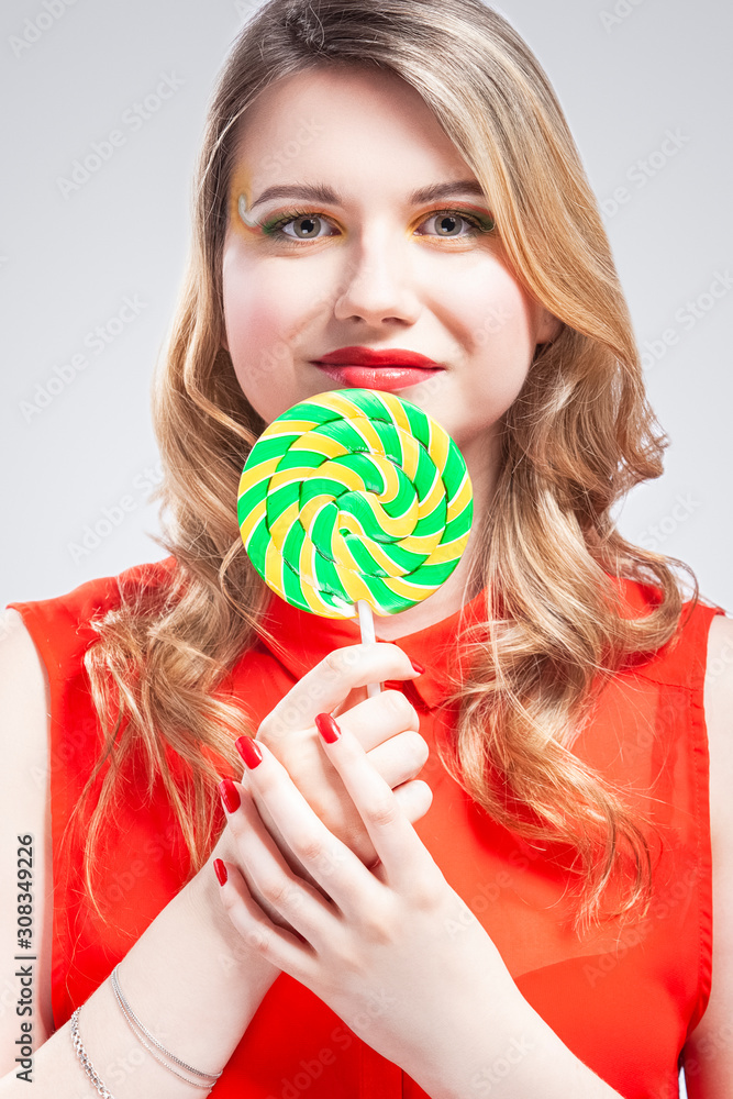 Portrait of Sexy Alluring Caucasian Blond Girl Eating Round Lollipop on Stick. Posing in Studio Against White.