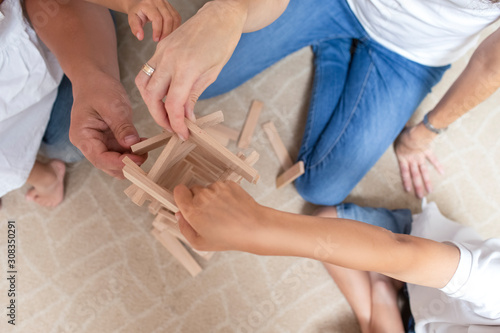 Family Values. Closeup of hands of  Caucasian Family with Kids Teaming Up While Building Tower of Wooden Tiles Indoors.