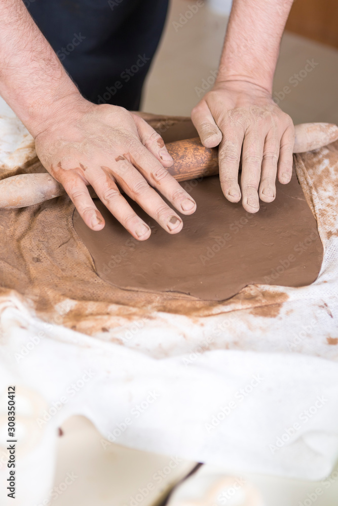 Pottering Ideas and Concepts. Closeup of Hands of Male Worker Rolling a Piece of Wet Clay on Table Before Moulding.