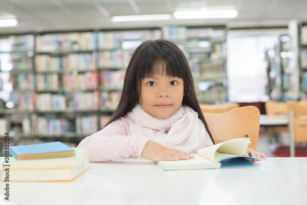 portrait of cute schoolgirl smiling while sitting with stack of books at table in library portrait of cute schoolgirl smiling while sitting with stack of books at table in library