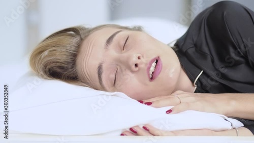 Woman can't sleep because noisy in home and turns from side to side puts a pillow on his head in bed resting attractive female lying tired beautiful morning dream relax slow motion