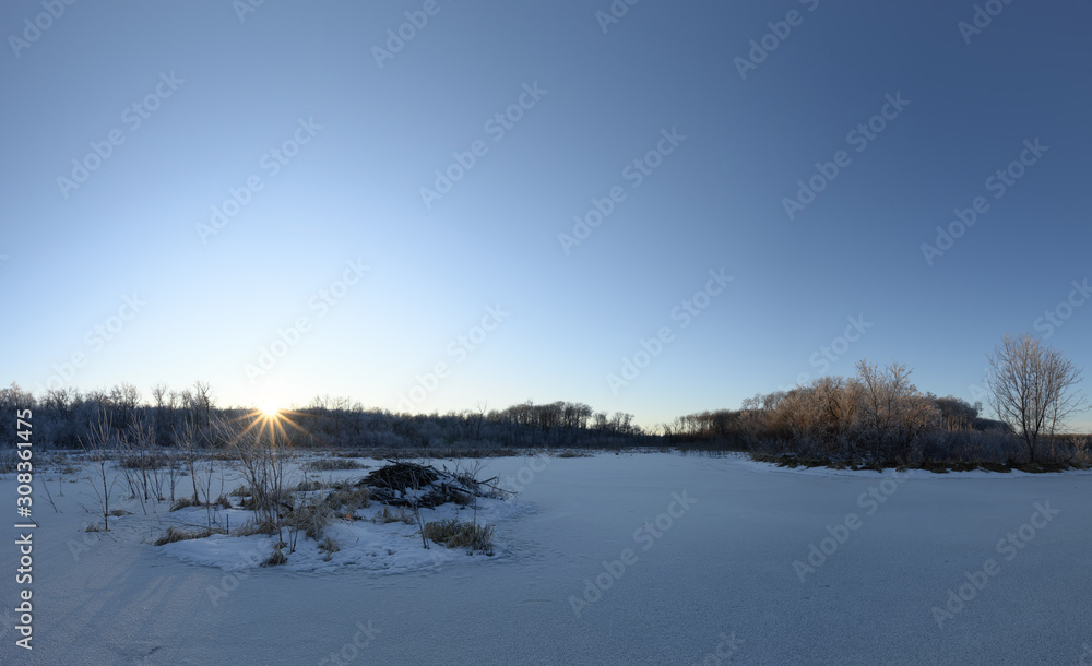 Scenic calm winter view of a frozen snow covered beaver pond with a sun star as the sun descends into the trees. Scenic calm winter view of a frozen snow covered beaver pond with a sun star as the sun descends into the trees.