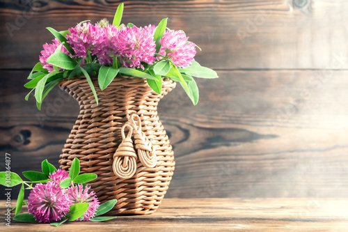 Bouquet of pink clover in a wicker vase on a wooden table on a summer morning