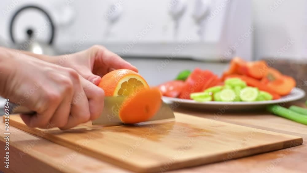 Woman using kitchen knife is cutting fresh orange on wooden board Woman using kitchen knife is cutting fresh orange on wooden board