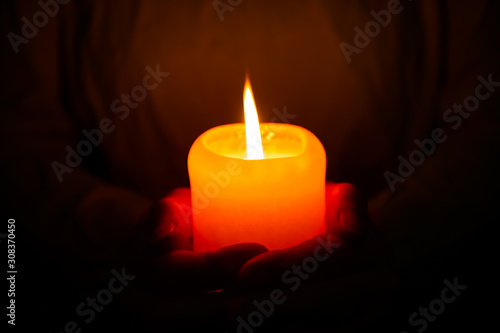 A person holding a glowing candle in the dark with both hands. Concept: hope and faith