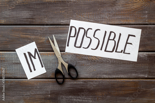 All is possible concept. Cut word impossible near scissors on dark wooden background photo