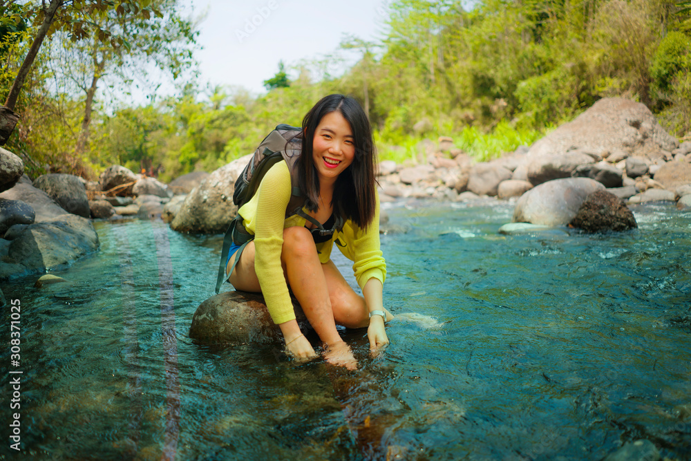 young beautiful and happy Asian Japanese woman carrying backpack trekking on mountains crossing river enjoying holiday nature and fresh environment hiking cheerful