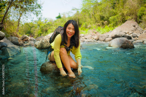 young beautiful and happy Asian Japanese woman carrying backpack trekking on mountains crossing river enjoying holiday nature and fresh environment hiking cheerful