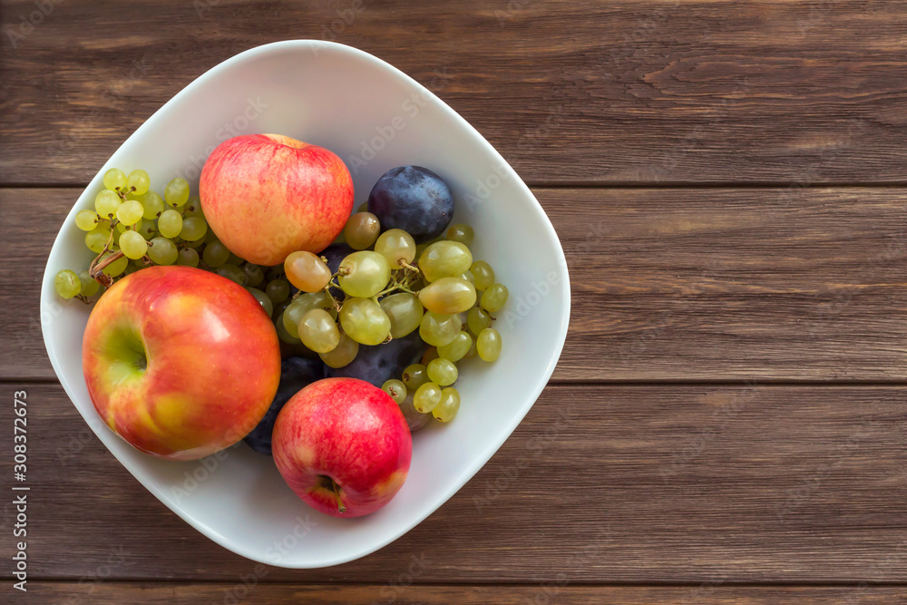 Fruits apples, grapes, plums in white plate on wooden background. Cooking, recipe, diet, healthy food concept. Top view, copy space Fruits apples, grapes, plums in white plate on wooden background. Cooking, recipe, diet, healthy food concept. Top view, copy space