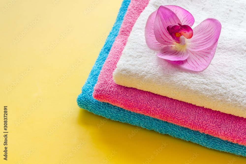 Clean towels - stack of laundred linen with orchid flower - on yellow background copy space Clean towels - stack of laundred linen with orchid flower - on yellow background copy space