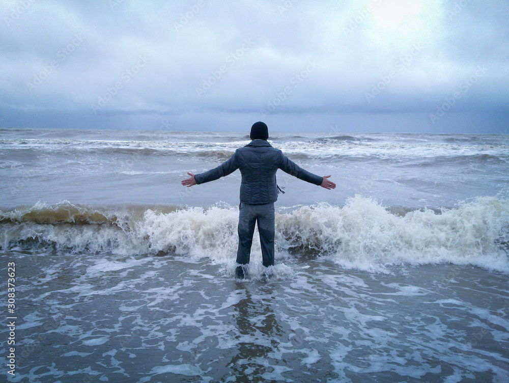 A man Standing in the stormy sea water. Man going out on winter sea beach. A man Standing in the stormy sea water. Man going out on winter sea beach.