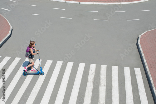 Girl carrying scooter and crossing road on way to school. Zebra traffic walk way in the city. Pedestrian passing a crosswalk. Healthy lifestyle. Eco-friendly transport. Safety concept for road users