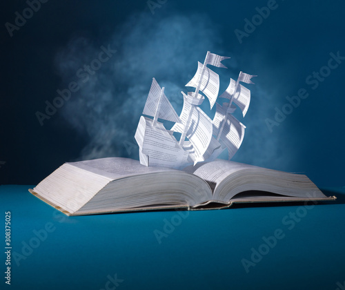 Sailing paper ship created from pages. Ship over an open book. Allegory of interesting contents of the book