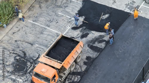 Time lapse of team of workers paving hot asphalt on a parking place . Small steamroller. Road construction workers with shovels in protective uniforms. Aerial, top view