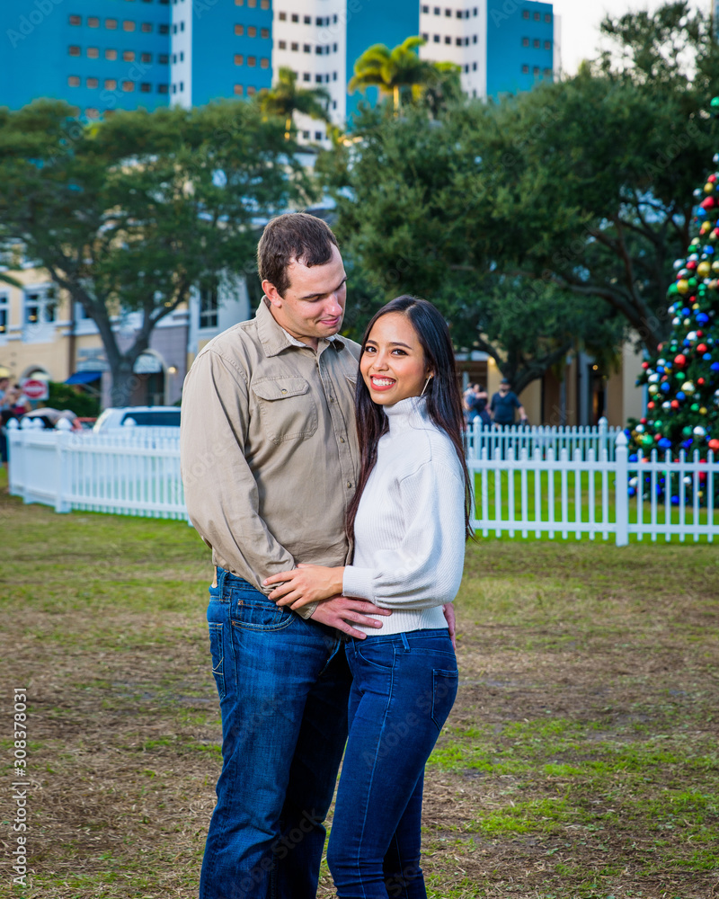 Happy young couple posing in front of the Christmas tree in a city park, Florida