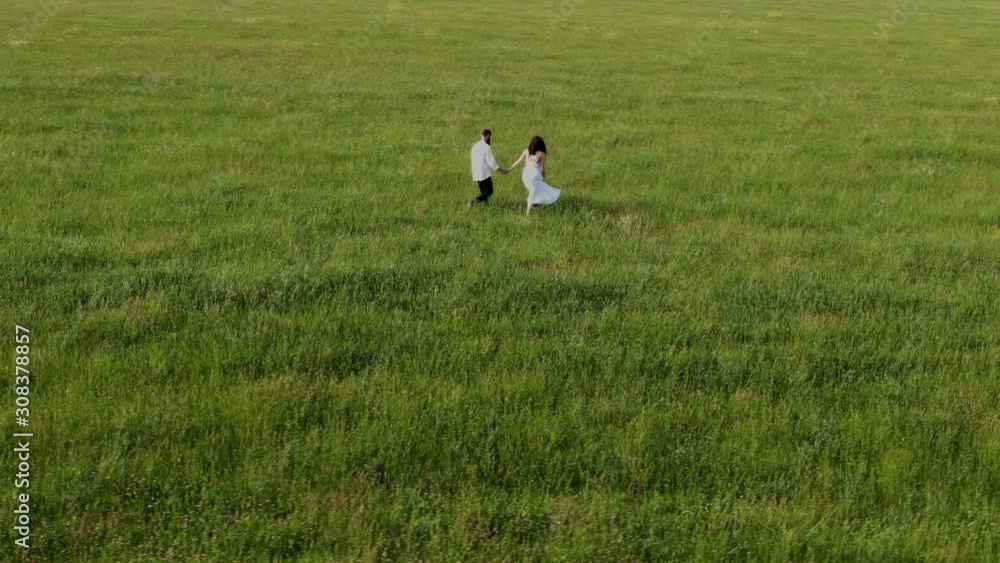 A man in trousers and a woman in a white dress walk on a green field