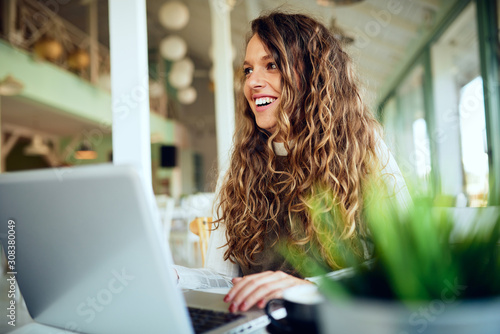 Attractive young curly brunette looking away and smiling in café