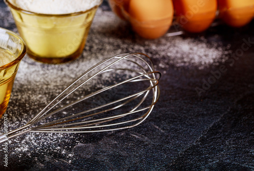 Making cake dough.Whisk, flour, sugar and eggs on black background.