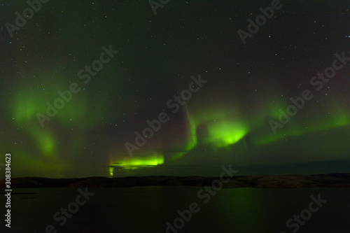 Northern lights over the lake and hills. Aurora at night in the sky in the north.