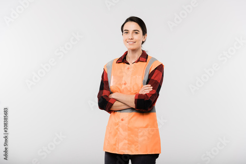 Happy young female engineer in workwear and orange jacket crossing arms by chest