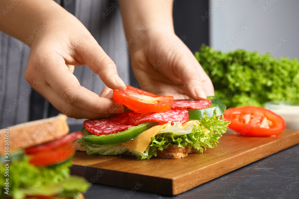 Woman adding tomato to sandwich at black table, closeup Woman adding tomato to sandwich at black table, closeup