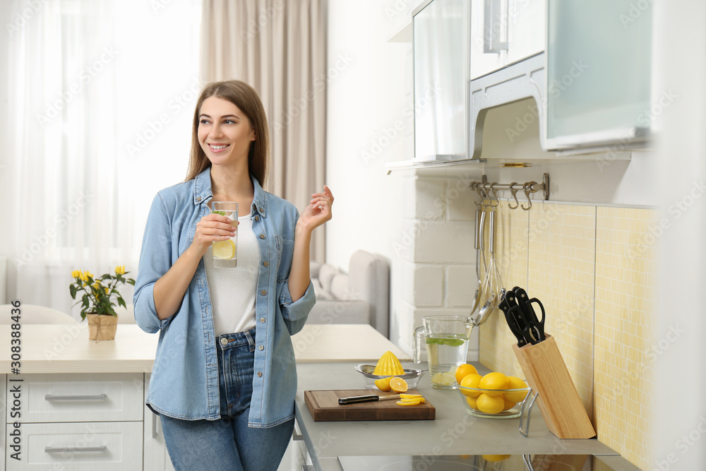 Young woman with glass of lemon water in kitchen Young woman with glass of lemon water in kitchen