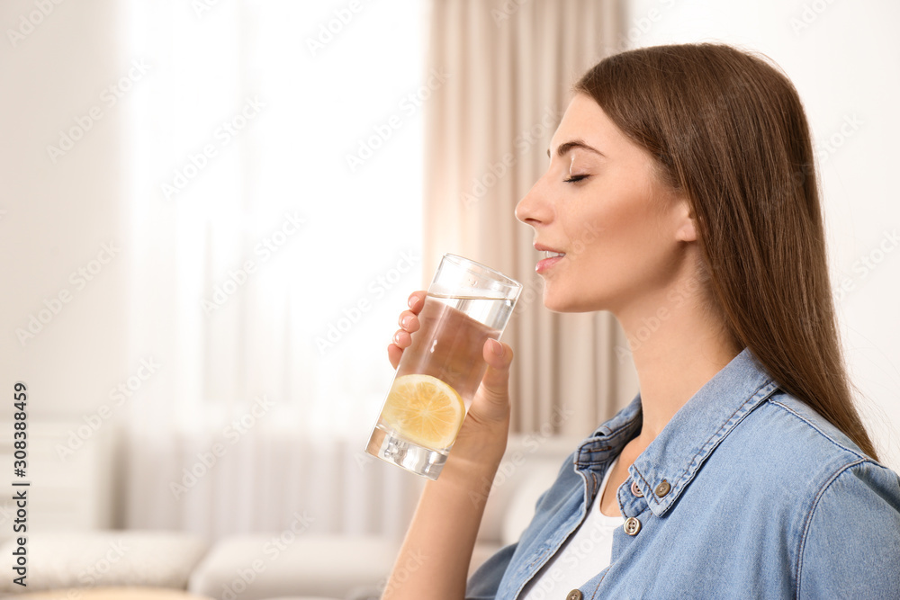 Young woman drinking lemon water at home. Space for text Young woman drinking lemon water at home. Space for text