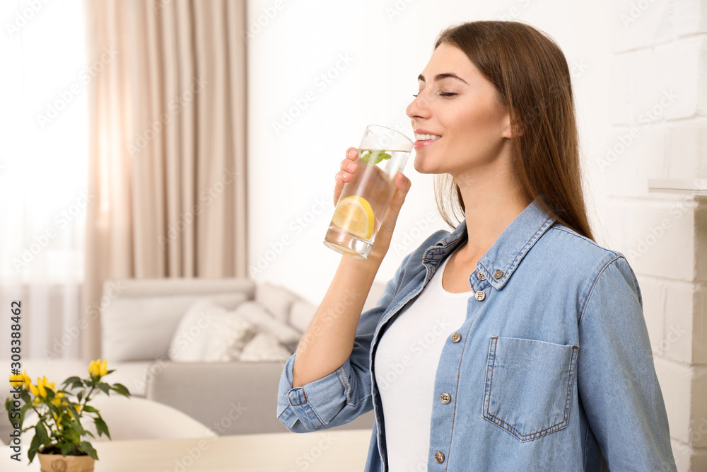 Young woman drinking lemon water in kitchen. Space for text Young woman drinking lemon water in kitchen. Space for text