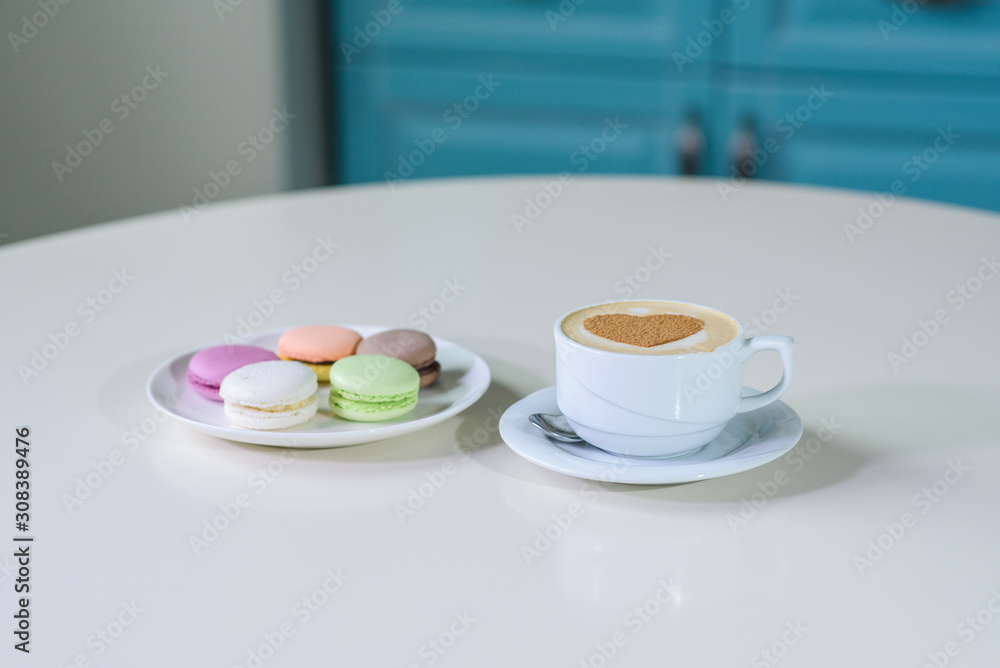 Delicious macaroons and cappuccino on a large bright table in a cozy coffee shop Delicious macaroons and cappuccino on a large bright table in a cozy coffee shop
