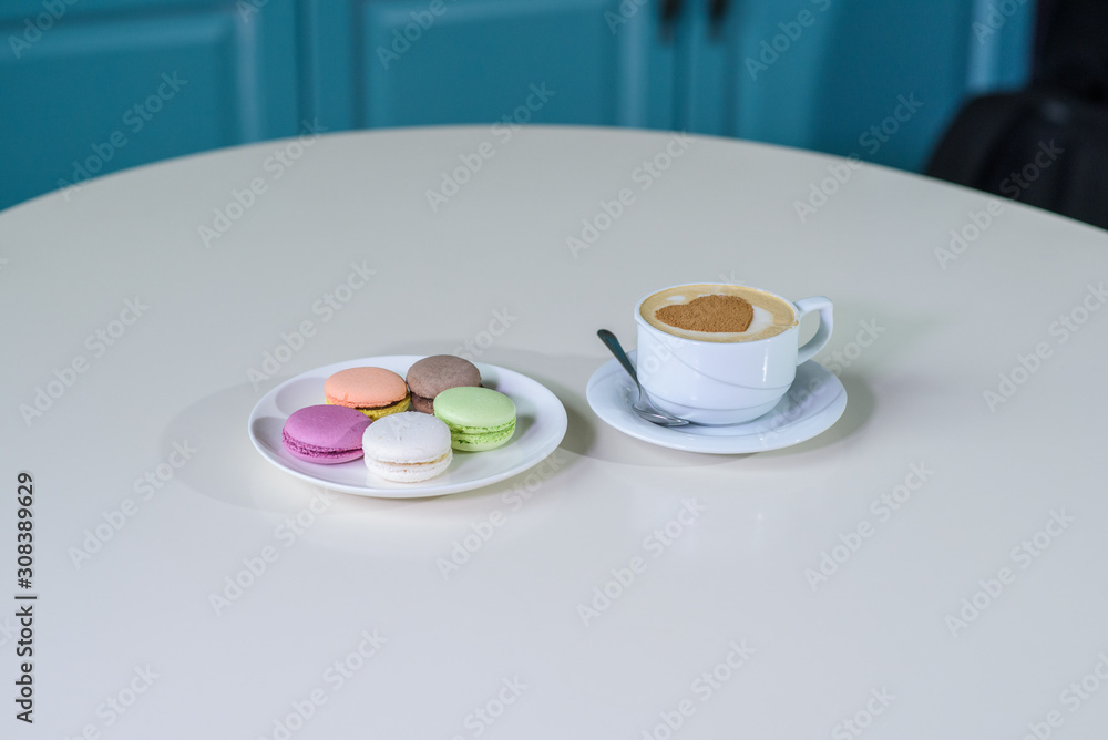 Delicious macaroons and cappuccino on a large bright table in a cozy coffee shop Delicious macaroons and cappuccino on a large bright table in a cozy coffee shop