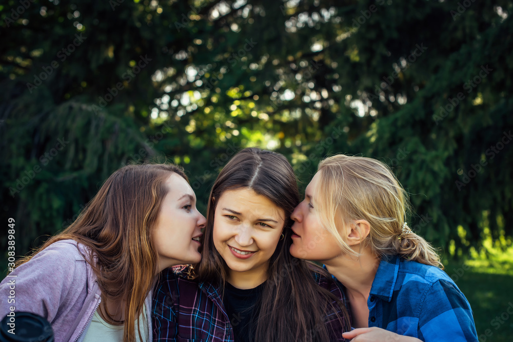 Portrait of three young girlfriends who whisper in the park. Exchange of news, emotional women whispering gossip. Portrait of three young girlfriends who whisper in the park. Exchange of news, emotional women whispering gossip.