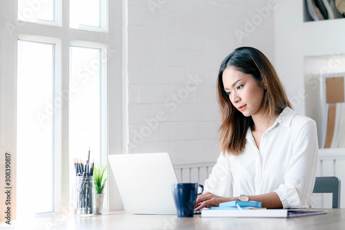 Portrait of young businesswoman looking at laptop screen while sitting at office desk in modern office. © NAMPIX