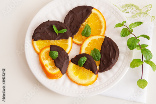 Candied orange in chocolate is a favorite Christmas treat for children and adults. Image of homemade candied orange dipped in chocolate with fresh mint. Top view