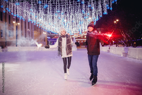 Winter skates, loving couple holding hands and rolling on rink. Illumination in background, night. Concept training