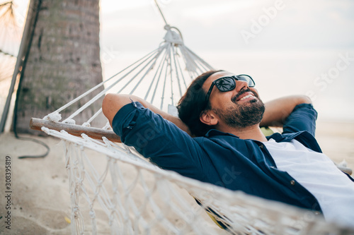Bild auf Leinwand A man enjoys calm, lies in a hammock on the background of the ocean and sunset