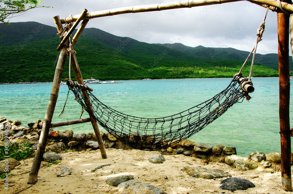 A place of rest and relaxation on the ocean. Hammock on posts on the ocean coast. Close-up. In the background a speedboat and jet ski, in the distance the coast of a tropical island.