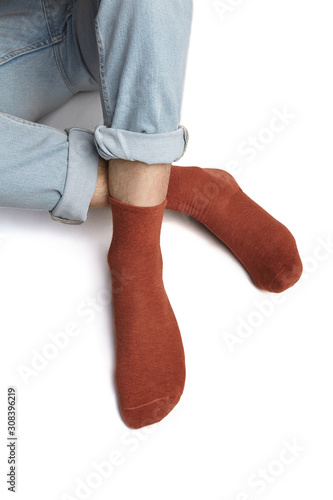 Cropped shot of a man's foots in blue jeans, lying on a white background. It is terracotta socks on his foots. 