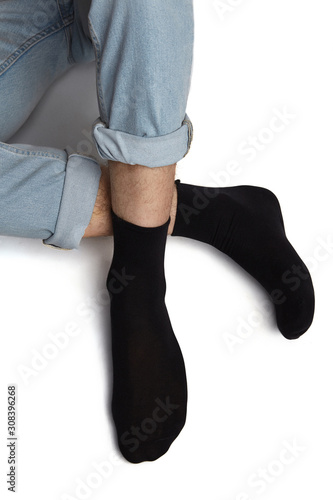 Cropped shot of a man's foots in blue jeans, lying on a white background. It is black socks on his foots. 