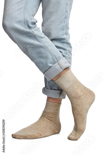 Cropped shot of a man's cross legs in blue jeans, staying on a white background. It is beige socks on his foots. 