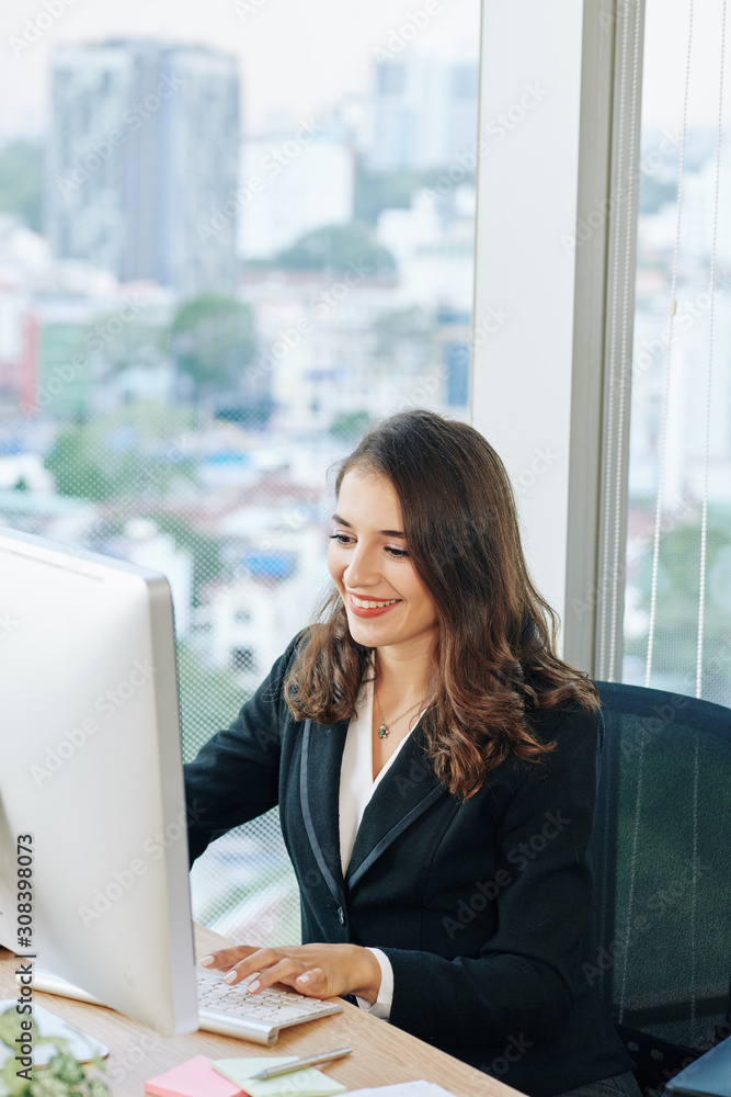 Pretty smiling young businesswoman enjoying working on computer at her office desk Pretty smiling young businesswoman enjoying working on computer at her office desk